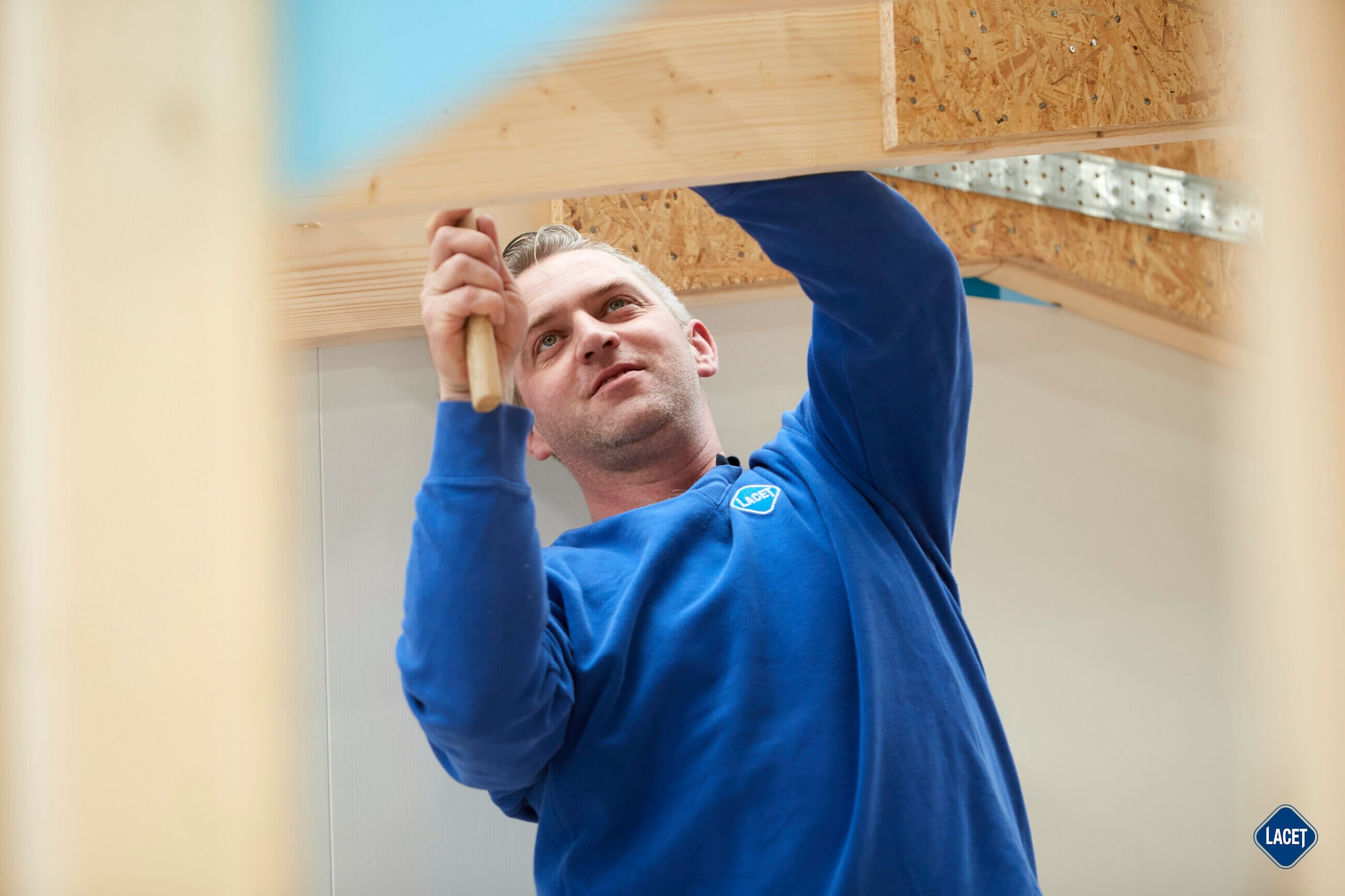 Ein Mann arbeitet an einem Holzbalken in einem Raum.